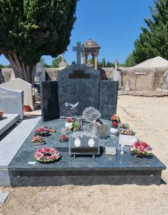 Grand monument funéraire familial en granit bleu-gris orné de fleurs au cimetière.