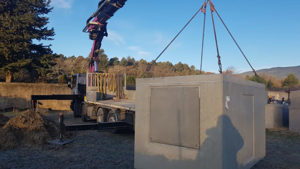 Pose d'un caveau funéraire monobloc en béton par camion grue au cimetière.