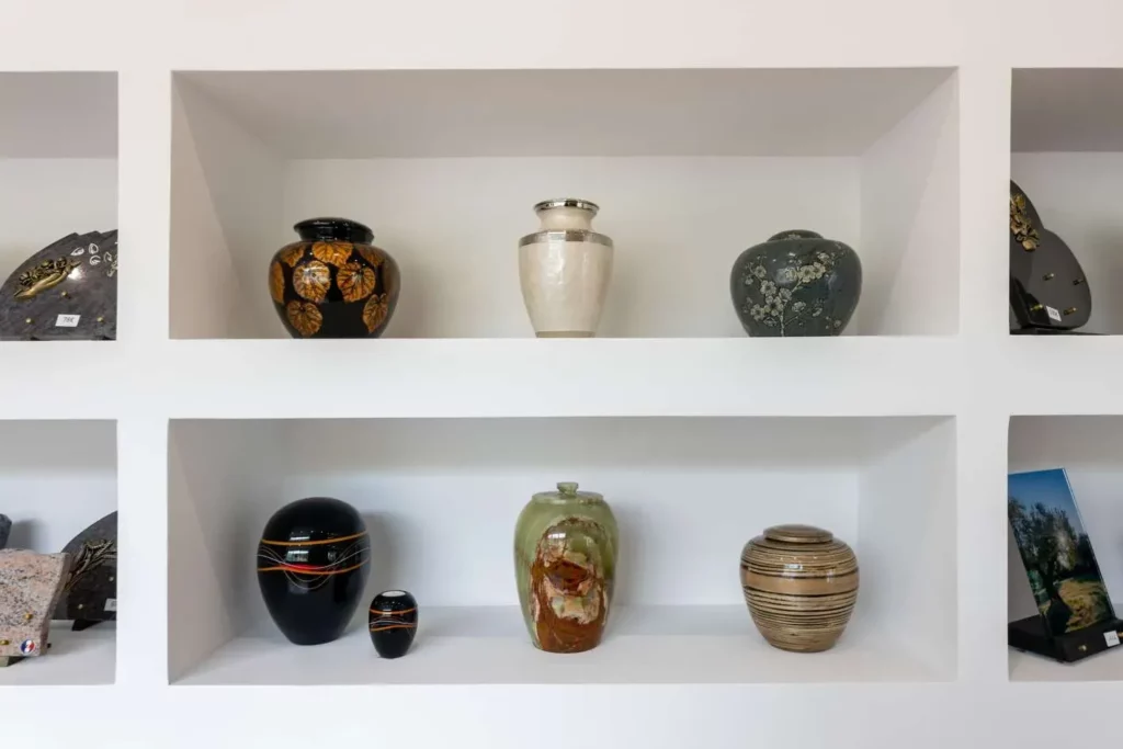 Exposition d'urnes funéraires de styles variés dans une niche d'un mur blanc.