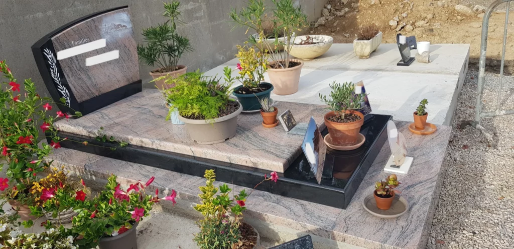 Monument funéraire personnalisé en granit rose et noir orné de plantes en pot.